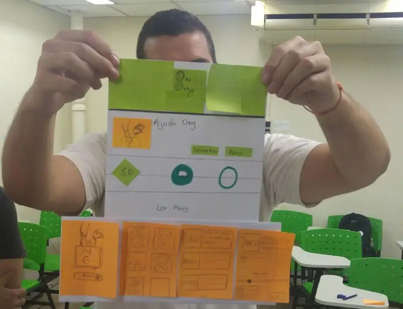 Homem segurando um papel A4 com vários post-its grudados nele simulando um aplicativo para celular.