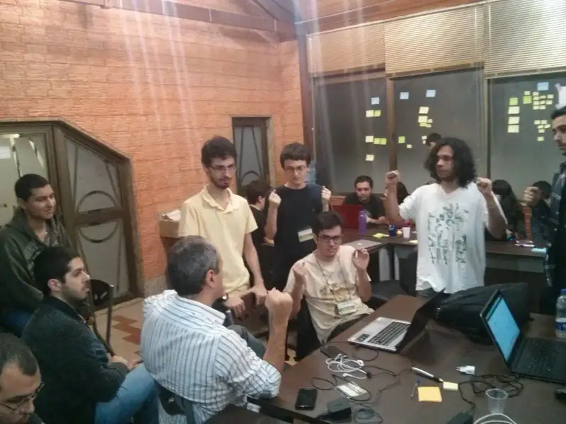 Um grupo de alunos em torno de alguns notebooks e celulares fazendo uma votação sobre qual direção o produto deles deveria tomar.