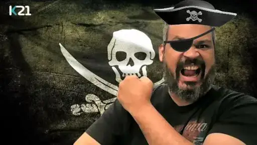 O logo da K21, uma bandeira de pirata tremulando ao fundo, nela uma caveira e abaixo dela duas espadas côncavas. Na frente, este humilde autor com um chapéu de pirata e um tapa-olho com o punho cerrado e braço dobrado em forma de L com o punho direito chegando ao ombro esquerdo. A expressão de grito de guerra no rosto com a boca aberta. Me descrevendo, homem, pardo, cabelos grisalhos, barba e bigode já grisalhos também com olhos castanhos escuros. Sinceramente, você não está perdendo muita coisa (risos).