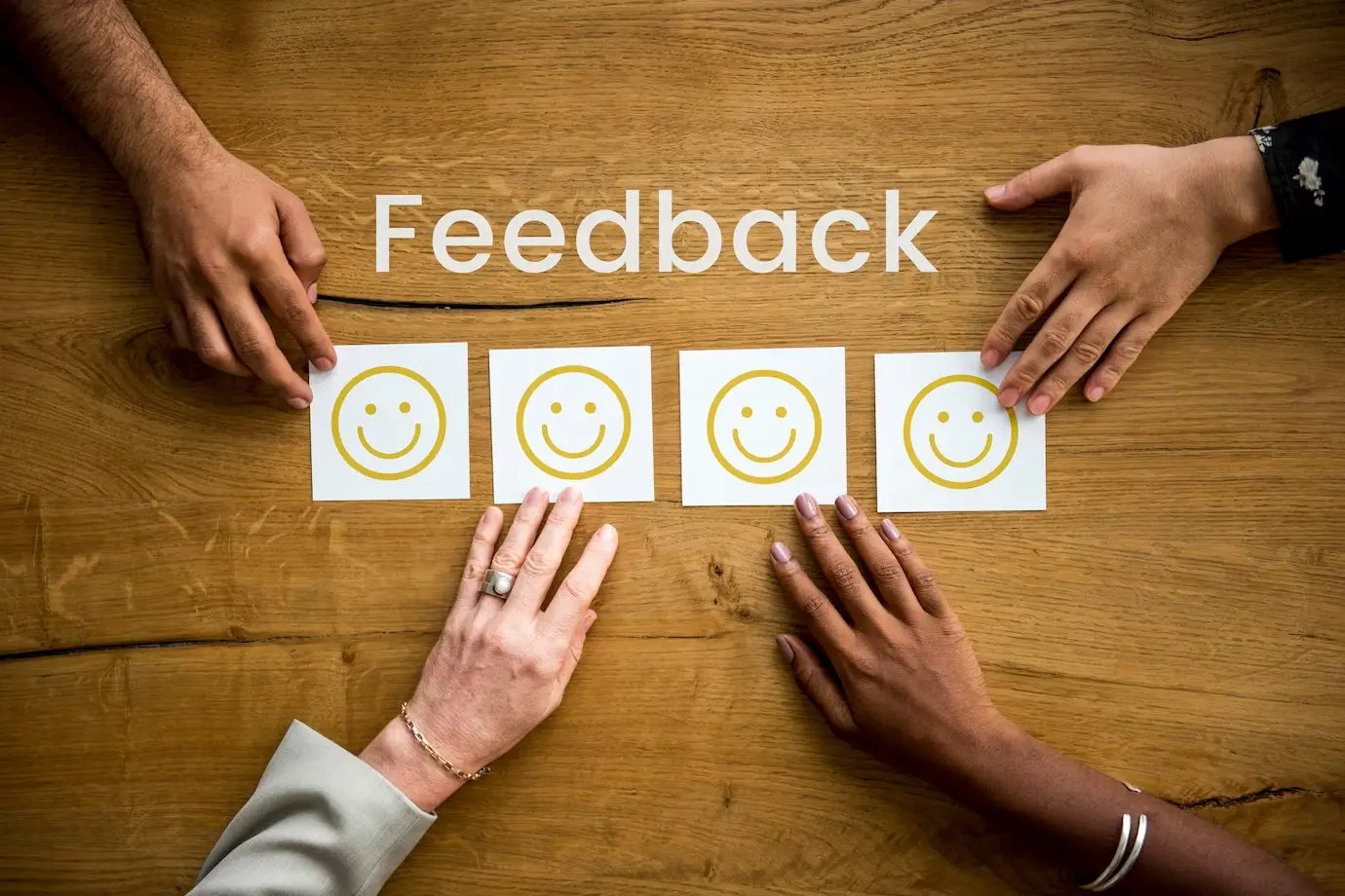 A palavra feedback. 4 papéis A4 com smiles amarelos e quatro mãos cada uma indo para cima de cada smile